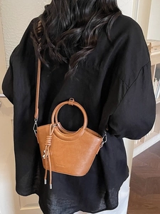 Sac seau marron avec poignée ronde et pompon, présenté sur un mannequin chic