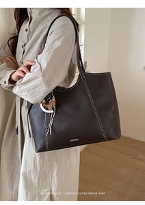 Detail of dark coffee leather tote bag with white contrast stitching and horse charm