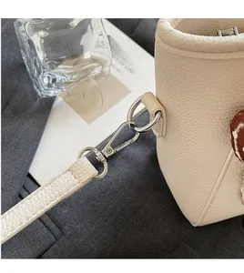Détail de la boucle en métal argenté et de la bandoulière en cuir d'un sac seau beige