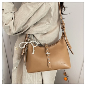 Detail of caramel brown dumpling bag featuring silver rivets and pearl bow charm