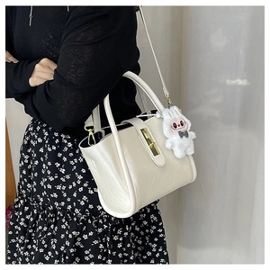 Détail d'un sac à main en cuir crème avec fermoir doré et accessoire en peluche blanche