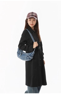 Sac hobo croissant en denim bleu clair avec boucles argentées porté par un mannequin en manteau