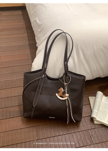 Close-up of a large dark brown leather tote bag with white stitching and horse pendant