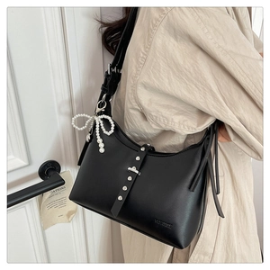 Detail of matte black hobo bag with silver studs and a pearl bow charm on model