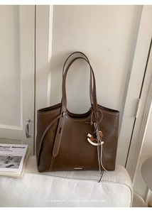 Detail of dark brown leather tote with white contrast stitching and horse pendant charm