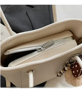 Close-up of silver metal zipper and decorative beaded charm on off-white leather tote bag