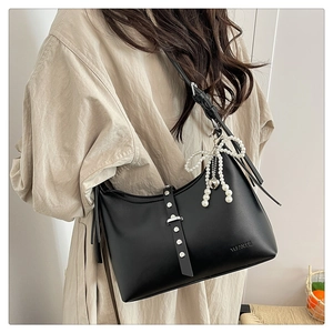Detail of black matte leather shoulder bag featuring rivet straps and pearl bow charm