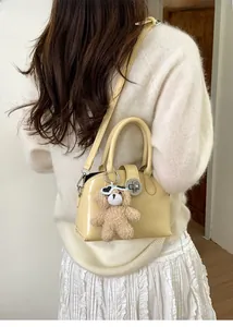 Detail of a beige vintage handbag with round metal lock and a cute brown teddy bear charm