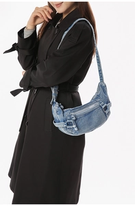 Détail d'un sac bandoulière en denim bleu en forme de croissant porté par un mannequin