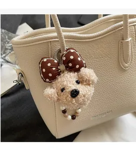 Close-up of fluffy puppy bag charm with bead necklace and bow on beige handbag