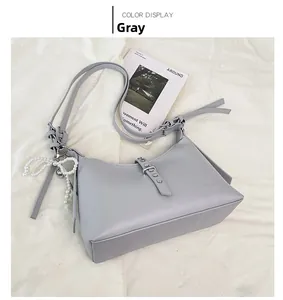 Detail shot of a grey crescent dumpling bag featuring a pearl bow pendant and matte finish