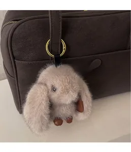 Close-up of a soft pink plush rabbit charm with golden ring on a brown leather bag