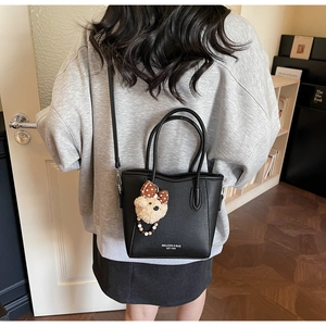 Detail of black pebbled leather tote bag with teddy bear charm and logo branding