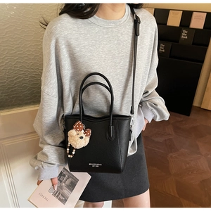 Detail of black pebbled leather tote bag with plush bear charm in a cozy indoor setting