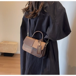Side view of bicolor brown leather handbag with fashion tag shown in indoor setting