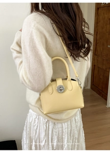 Detail of light yellow leather handbag with silver rotary lock and round top handle