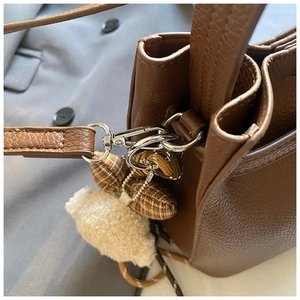 Dettaglio borsa a secchiello in pelle marrone con orsetto di peluche e ciondolo a quadri
