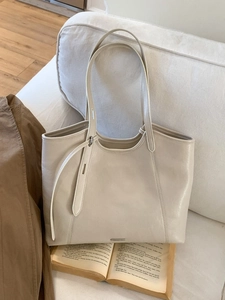 Minimalist beige leather tote bag with long straps on a sofa, large capacity for work