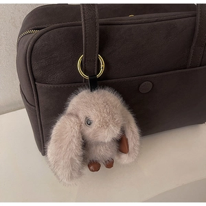 Detail of a fluffy beige bunny pendant with long ears on a dark brown handbag