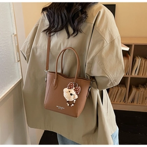 Brown litchi grain bucket bag with teddy charm shown on shoulder by a model