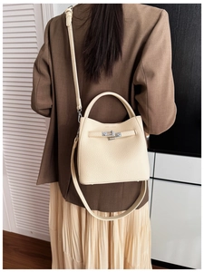 Detailed view of beige lychee leather bucket bag with metal buckle on a model