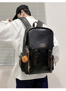 Detail view of the black leather backpack side profile with brown straps and bear charm