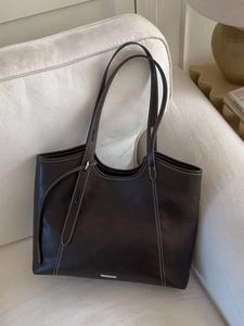 Dark brown large leather tote bag with white contrast stitching on beige sofa