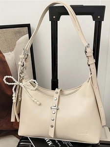 Minimalist beige dumpling shoulder bag with metal rivets and a pearl bow charm decoration