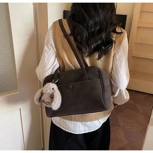 Close-up of a dark coffee vintage leather shoulder bag with a cute plush bunny charm