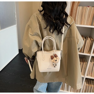 Detail of cream pebbled leather mini tote bag with teddy bear charm and brand logo