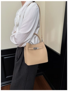 Close-up of light beige leather handbag featuring silver metal twist lock and texture