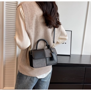 Detail of color-block handbag with metal hardware and strap worn by a model in a room