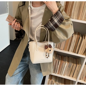 Detail of off-white lychee pattern leather bucket bag with cute plush bear charm