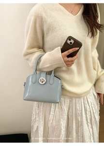 Detail of light blue glossy leather handbag with circular silver clasp and dual handles