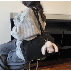 Detail of a black leather tote bag with a cute plush bunny charm worn by a model