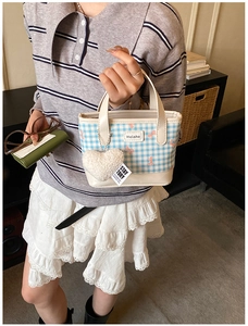 Détail du sac seau à carreaux bleus avec nœud rose et breloque cœur sur la poignée cuir