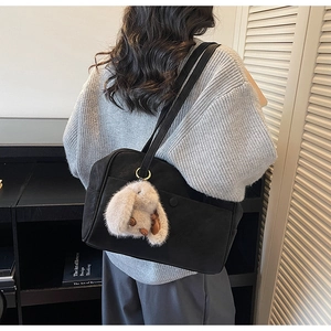 Detail of black leather shoulder bag with plush rabbit ear charm worn by model