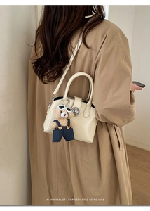 Dettaglio di una borsa minimalista in pelle crema con ciondolo a orsetto e chiusura in metallo