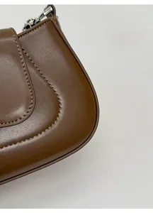 Detailed close-up of dark brown textured leather and stitching on the underarm bag
