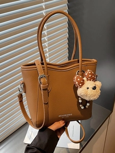Brown lychee leather bucket bag with top handles, crossbody strap and plush bear charm