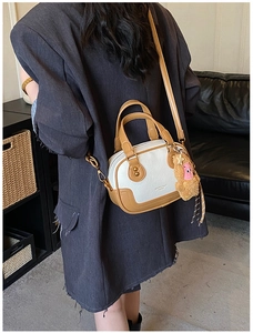 Detail of a white and brown contrast crossbody bag featuring a plush monkey charm accessory