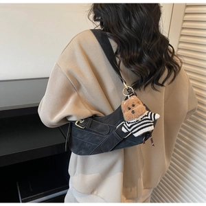 Detail of black suede saddle bag featuring industrial metal buckle and a cute bear charm