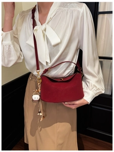 Detail view of burgundy leather underarm bag with cute plush animal charm on a model