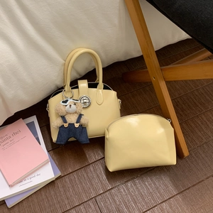 Set borsa a mano giallo crema con ciondolo orsetto e pochette su pavimento in legno