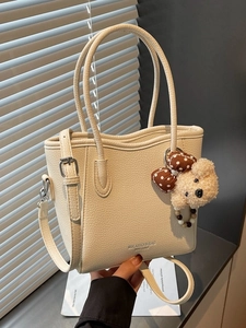 Chic beige lychee leather bucket bag with top handles, shoulder strap and a cute bear charm