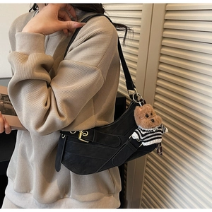 Detail view of a black saddle bag with metallic buckle and a cute bear plush pendant charm