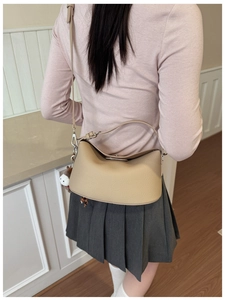 Rear view of model wearing beige pebbled leather underarm bag with plush charm accessory