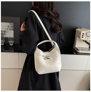 Détail d'un sac seau en cuir blanc crème avec boucle argentée nouée sur un manteau noir
