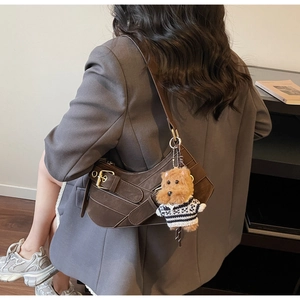 Detail of dark brown suede crescent bag with metal buckle and plush doll accessory