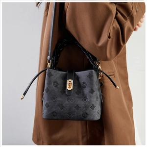 Grey embossed bucket bag with gold lock shown on model wearing a brown blazer jacket